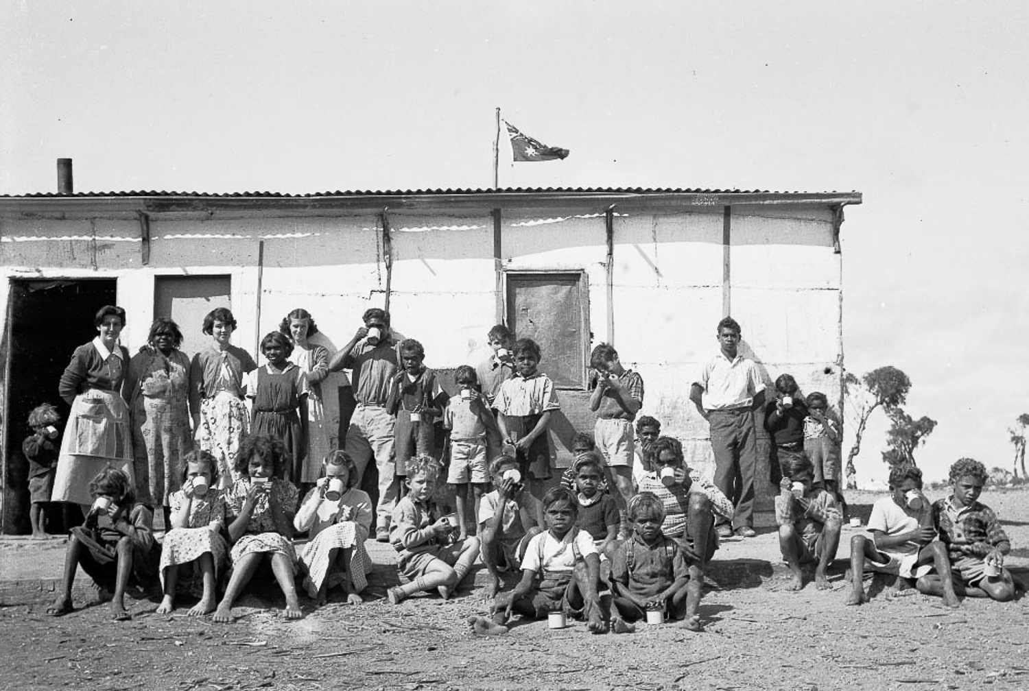 ‘Cocoa time’ at Cundeelee mission, outside the kitchen under the Australian flag. The Cundeelee mission would be eventually closed in 1985, and in 1986, elders would return to their original homelands on Spinifex Country to the east, and establish the community of Tjuntjuntjara.