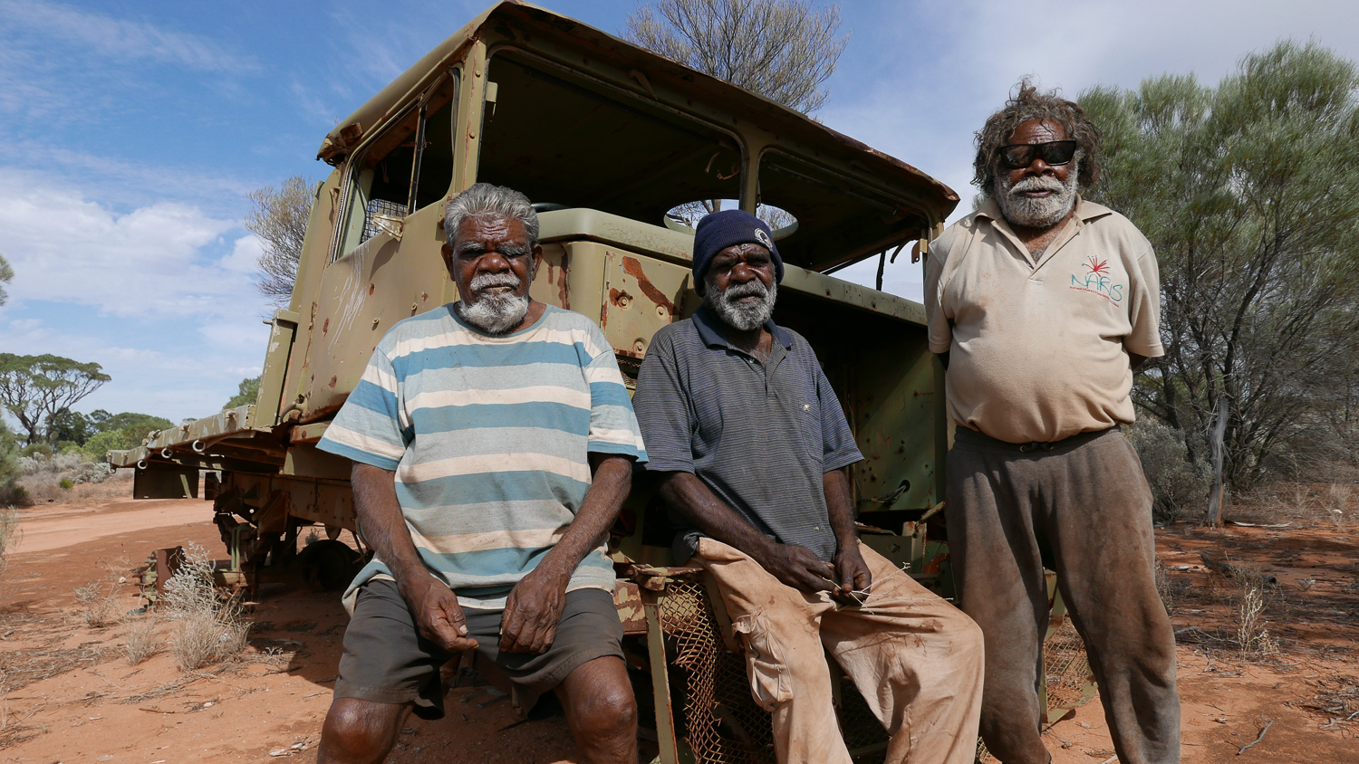 Fred Grant, Rusty Hogan and Ned Grant, with the army truck they travelled in to return to Spinifex Country and establish Tjuntjuntjara community. Fred and Ned were part of the original group of people who were ‘found’ in the bush and relocated to Cundeelee mission. In the late 1980’s they returned to Spinifex Country, because they “wanted to be home”, and to be able to continue to speak their original language and practice their culture. 