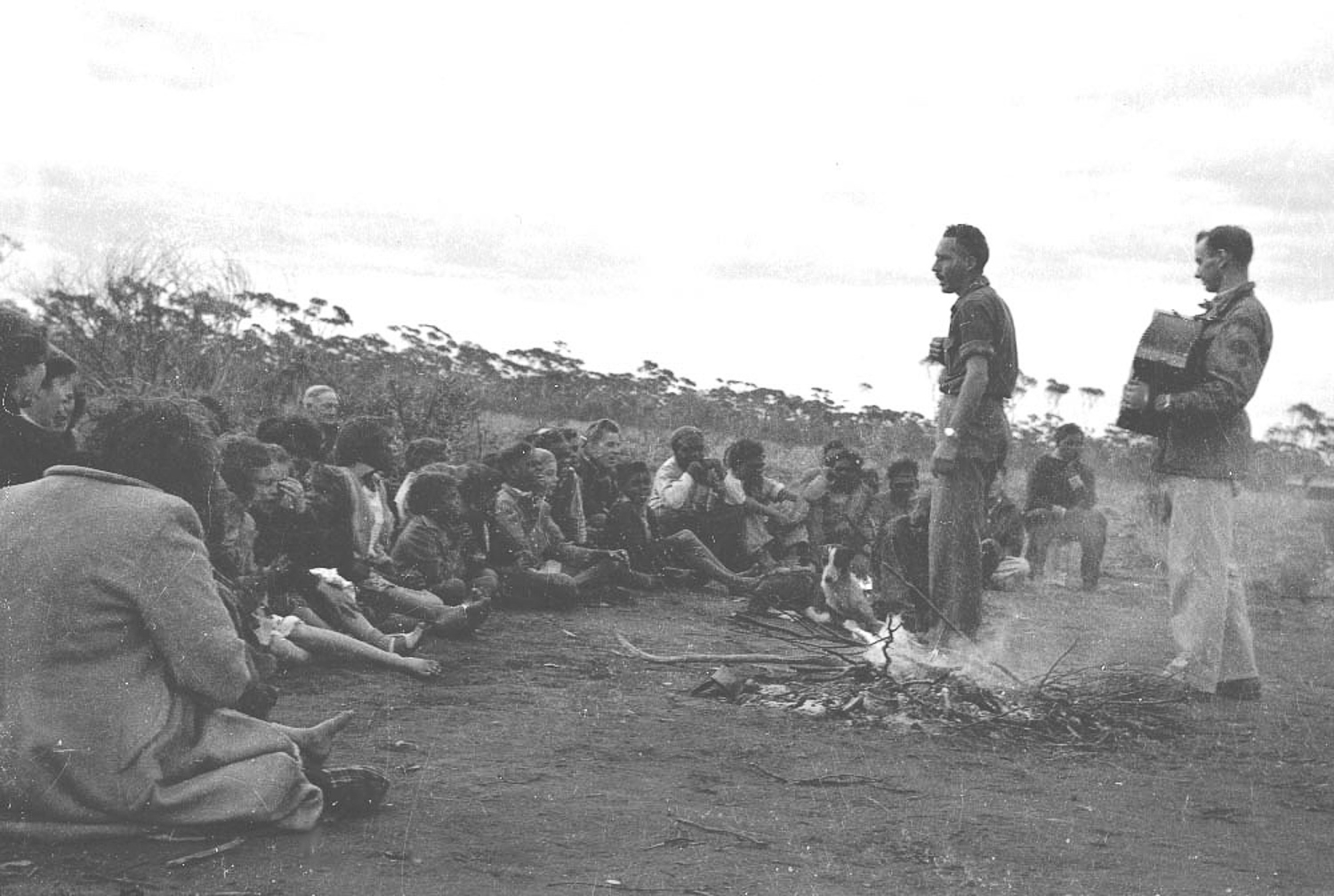 A church camp meeting at Cundeelee, led by missionary, teacher and photographer Robert McKeich. Anangu would set up bush camps around the mission site, and would be visited by missionaries who would hold church services in an attempt to convert Anangu to Christianity.