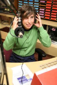 colour photo of a young woman sitting at a radio desk with headphones on