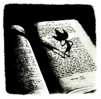 A book lies open on a table. Standing on the pages of the book is a small black character with three points on its head.