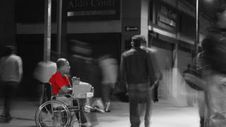 Man in wheelchair wearing red shirt, in black and white scene