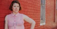 Clementine Ford wearing pink shirt standing in front of brick wall