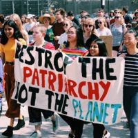 Crowd of young female protesters holding a sign that says "Destroy the patriarchy not the planet"
